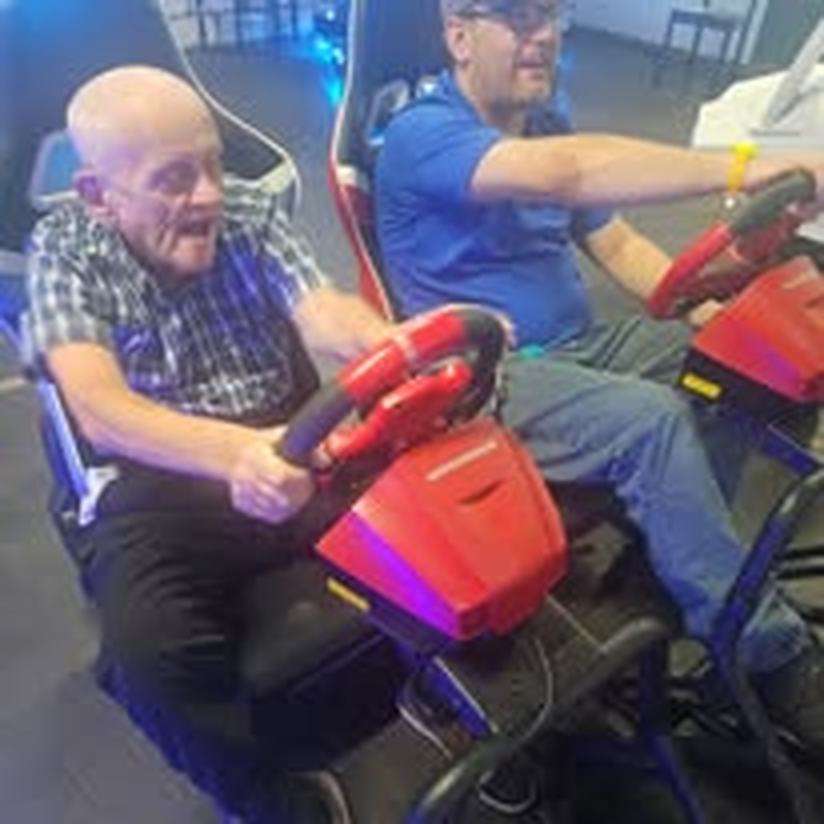 Two individuals racing side by side on arcade driving simulators.