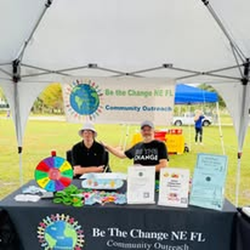Two staff members at the Be The Change NE FL outreach table.